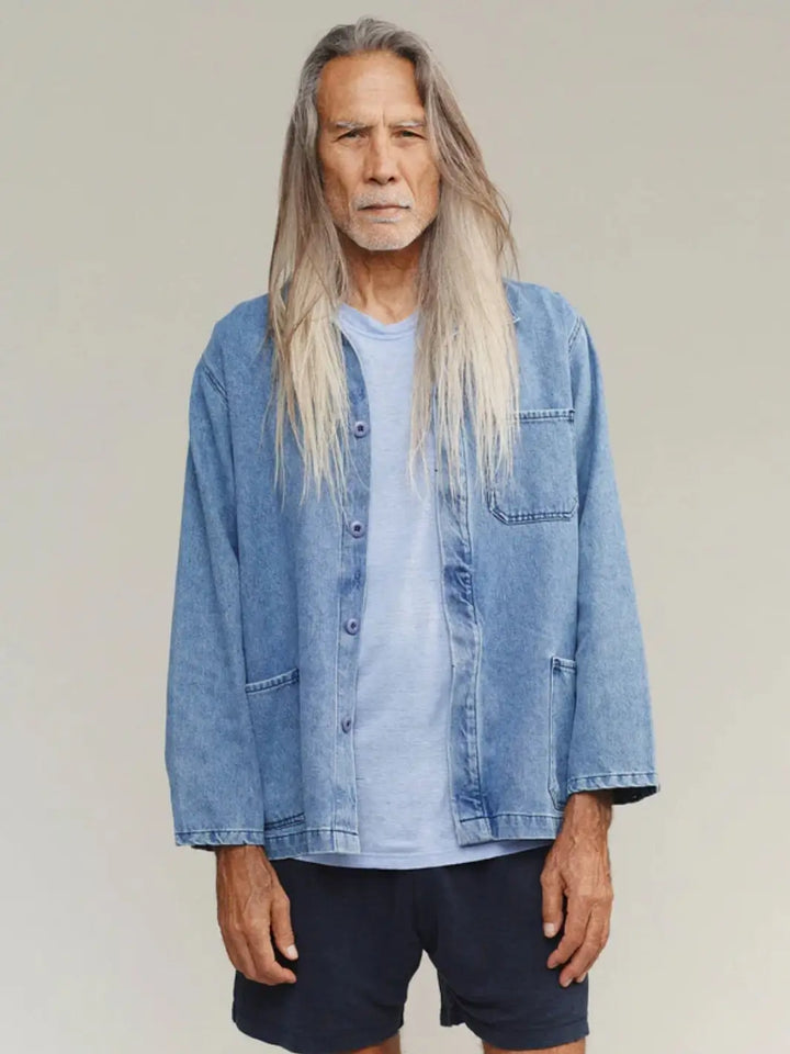 A medium shot captures a model with long hair wearing the relaxed-fit Jungmaven Denim Olympic Jacket in Light layered over a light blue crewneck tee and dark shorts | Twentyseven Toronto
