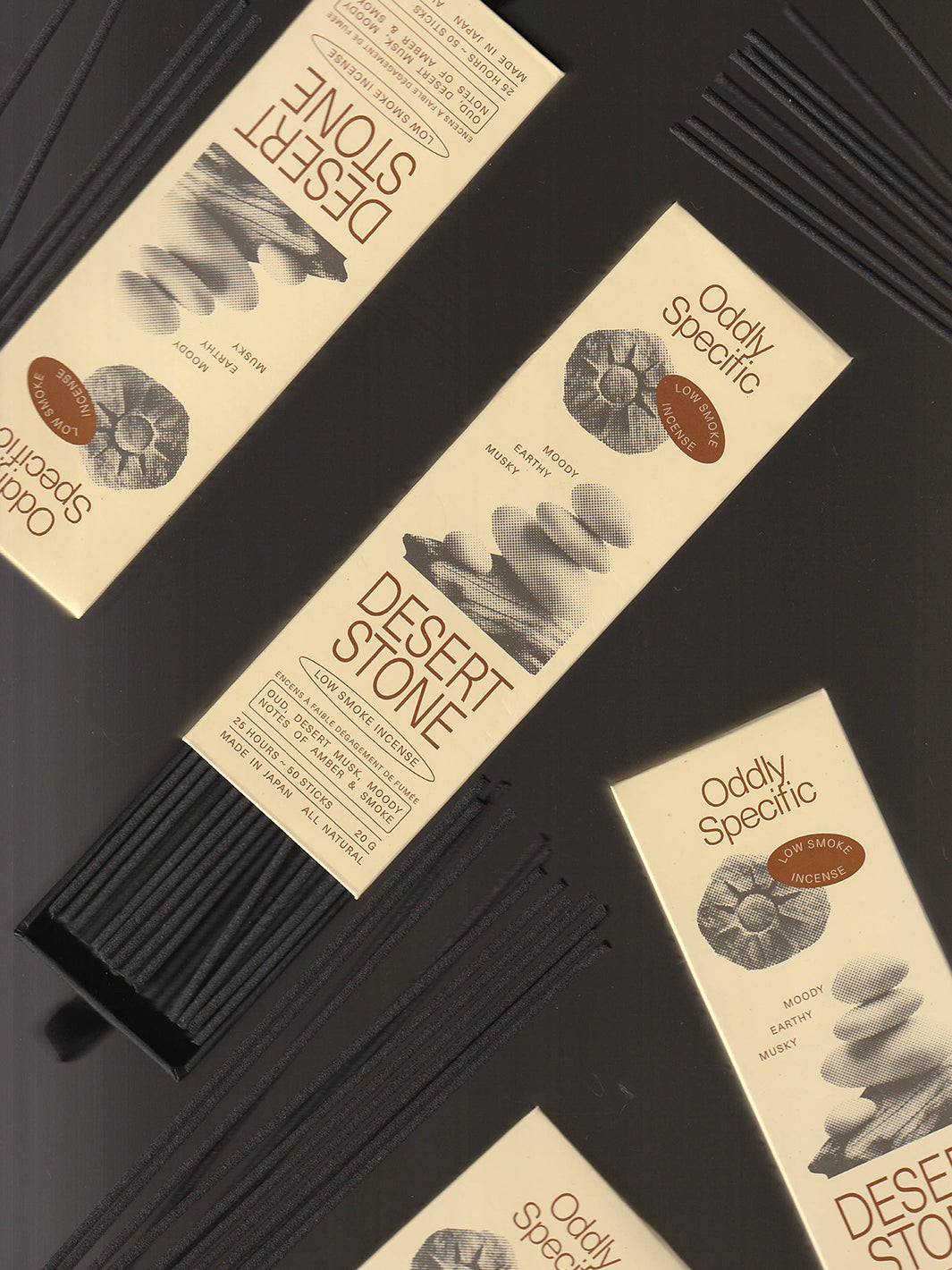 Flat lay of Oddly Specific Desert Stone Japanese incense featuring beige packaging with brown lettering, black incense sticks and illustrated desert stones on a dark background | Twentyseven Toronto