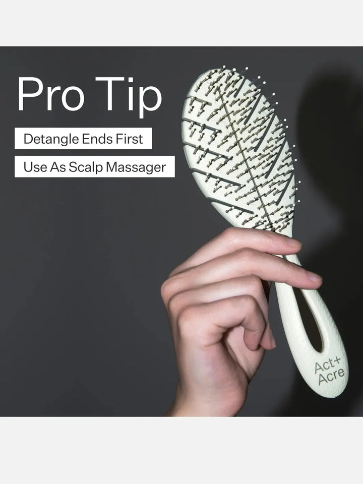Hand holding a light green Act+Acre Detangling hairbrush with 'Pro Tip' text on a dark background | Twentyseven Toronto