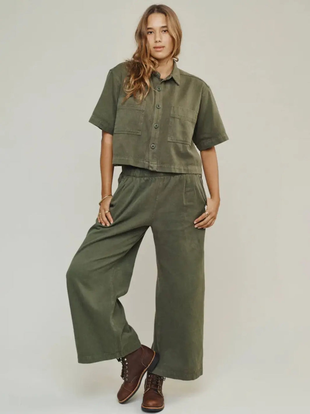 A model poses from the front wearing a matching olive green utility shirt paired with the loose-fitting Jungmaven Disco Twill Pant - Olive Green and brown leather boots | Twentyseven Toronto