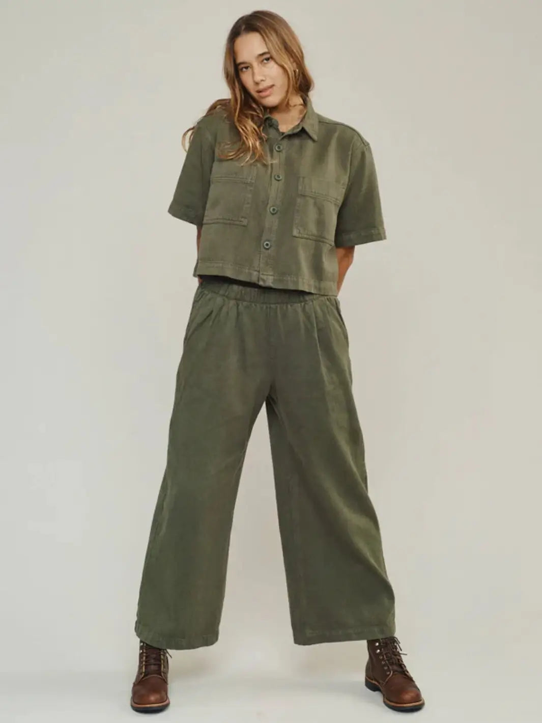 A full-length view shows a model standing with hands behind her back, showcasing the comfortable silhouette of the Jungmaven Disco Twill Pant - Olive Green | Twentyseven Toronto