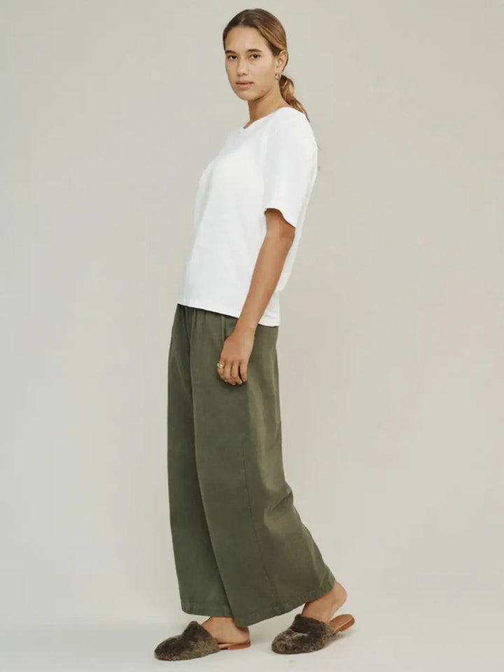 A side profile shot captures a model wearing a classic white t-shirt styled with the wide-leg Jungmaven Disco Twill Pant - Olive Green and fuzzy brown slippers | Twentyseven Toronto