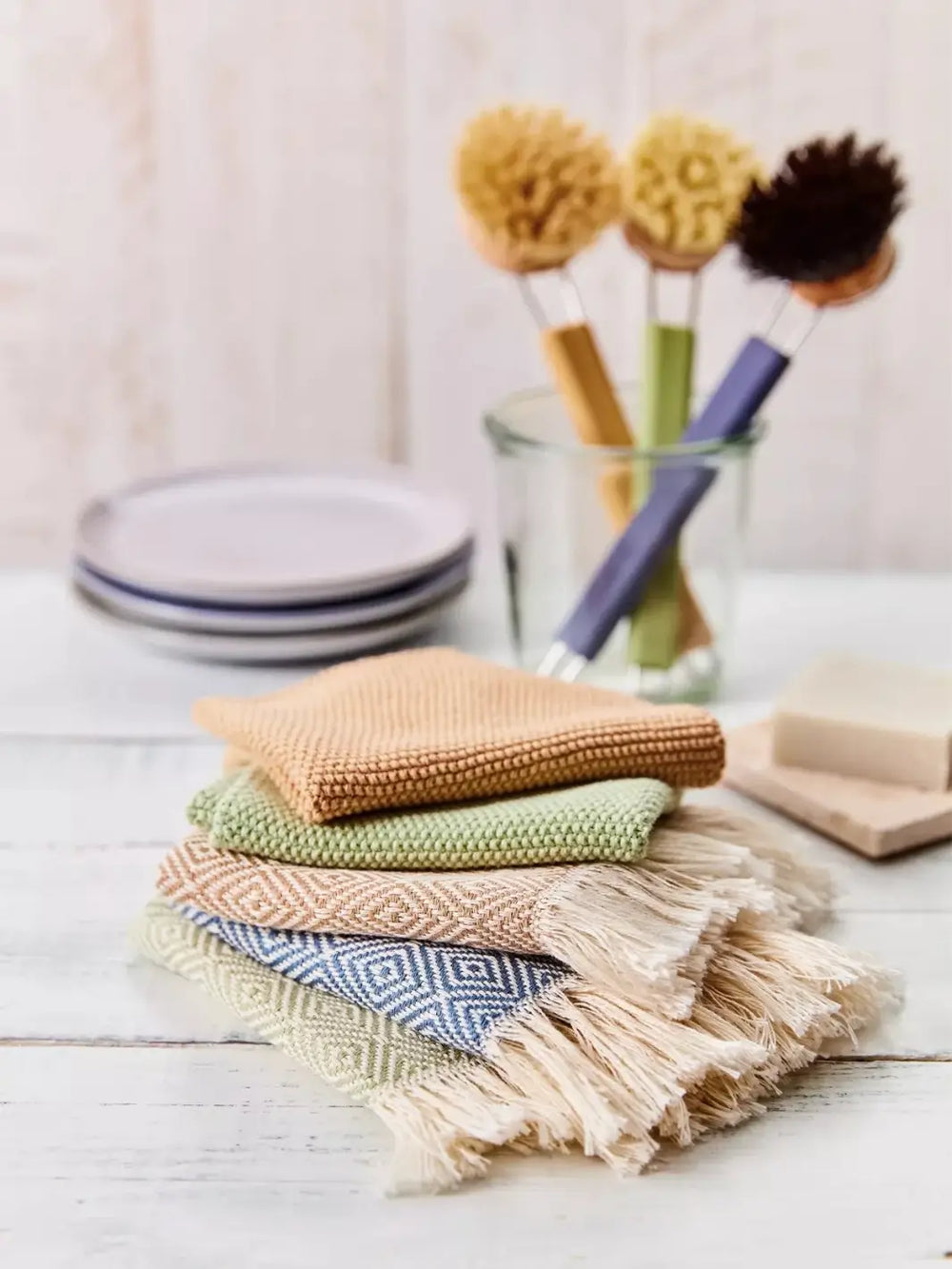 Stack of colourful knitted dishcloths on a wooden surface with cleaning brushes from Burstenhaus Redecker in the background | Twentyseven Toronto