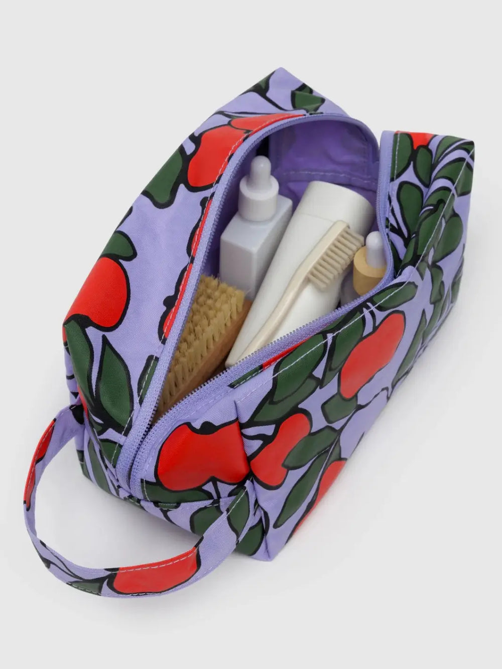 An open BAGGU Dopp Kit in Apple Tree with a purple interior is filled with toiletries, including brushes and white bottles | Twentyseven Toronto