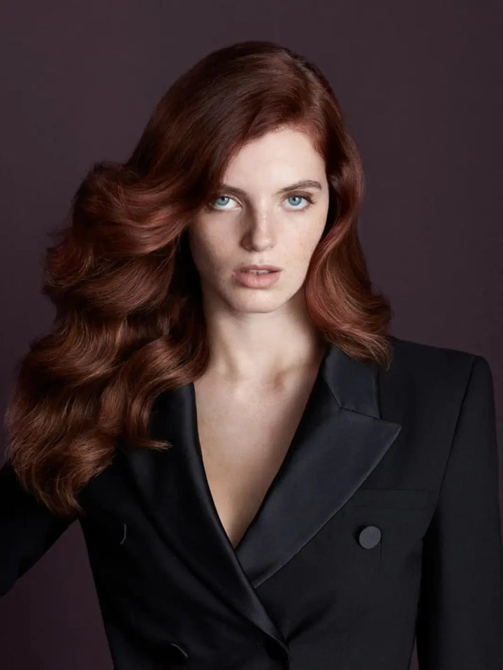 A portrait of a woman with voluminous, glossy brunette waves styled using Hair by Sam McKnight Dressed to Kill Define and Defrizz Creme while wearing a black blazer | Twentyseven Toronto
