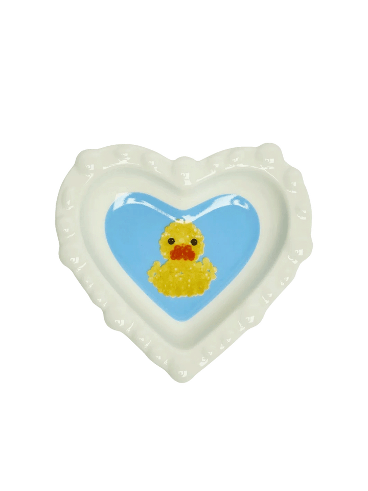 Fishs Eddy x Susan Alexandra Duckie Dish featuring a yellow duck on a blue heart-shaped centre with scalloped white edges | Twentyseven Toronto