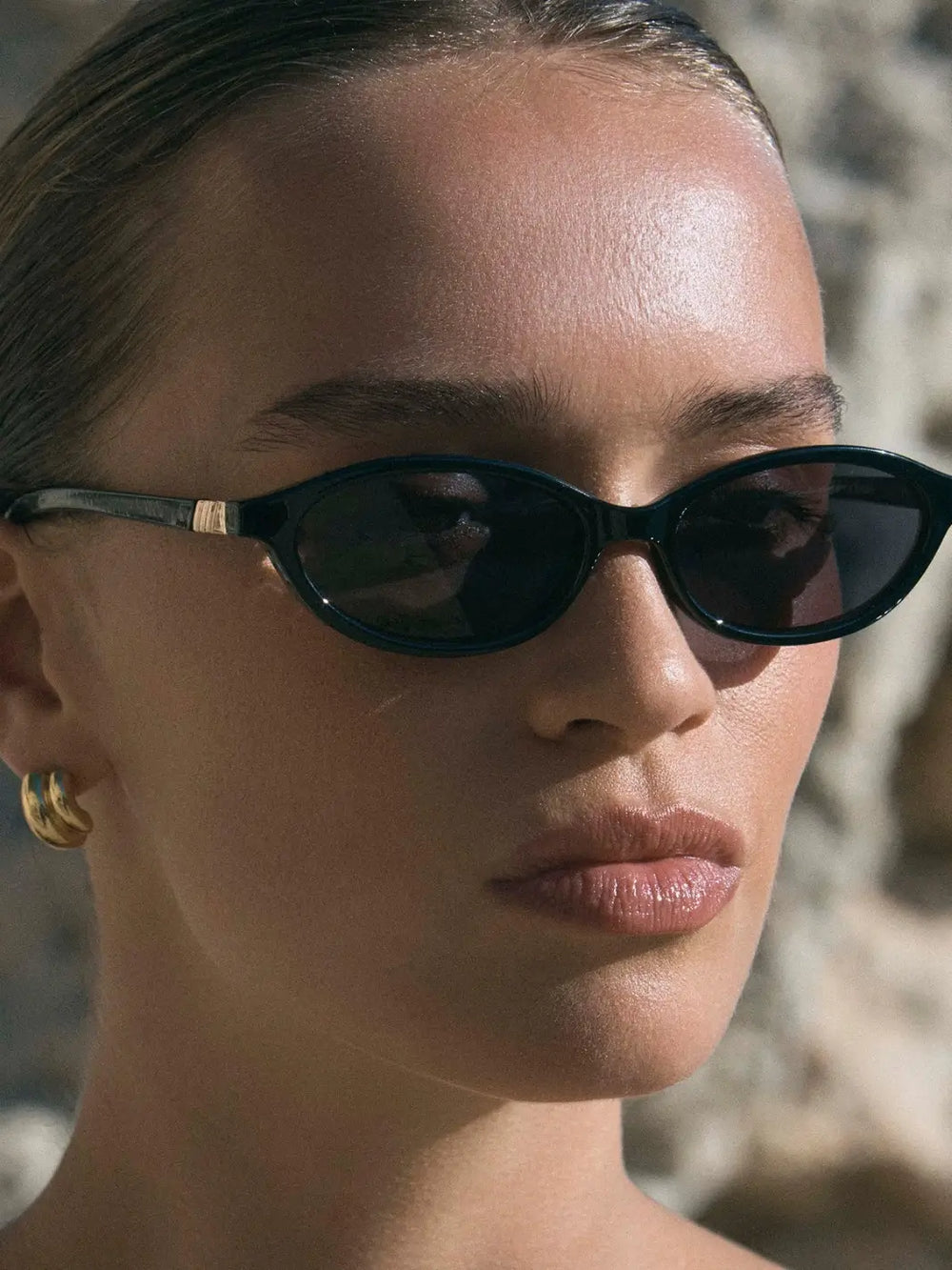 A woman modeling the slim, oval-shaped Le Specs Duskfall - Black Smoke Mono sunglasses in an outdoor setting | Twentyseven Toronto