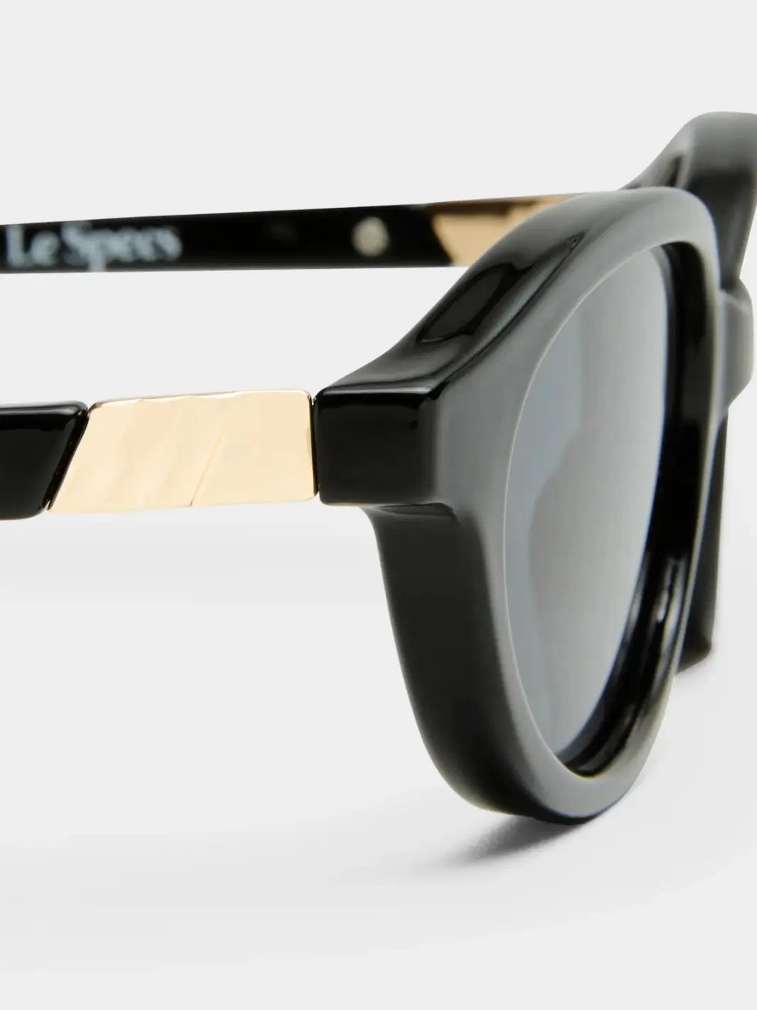 A macro close-up highlighting the textured gold metal piece connecting the front frame and temple arm of the Le Specs Duskfall - Black Smoke Mono sunglasses | Twentyseven Toronto
