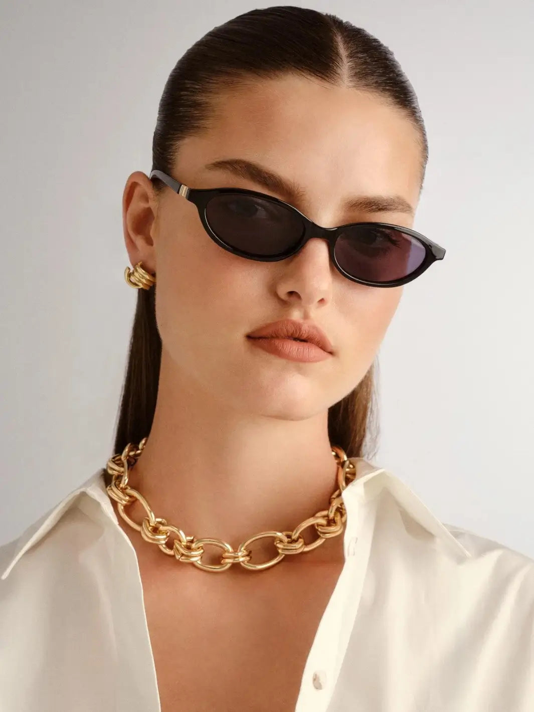 A woman looking forward while wearing the sleek Le Specs Duskfall - Black Smoke Mono sunglasses paired with a gold chain necklace | Twentyseven Toronto