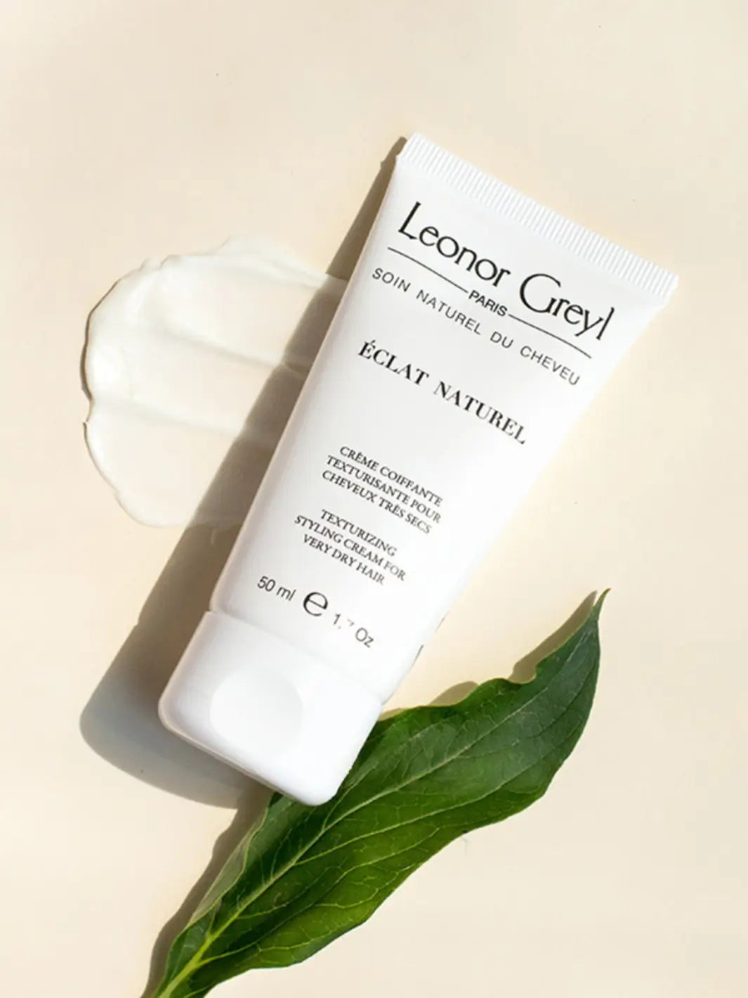 Tube of Leonor Greyl 'Éclat Naturel' with a leaf and product texture swatch on a beige background | Twentyseven Toronto