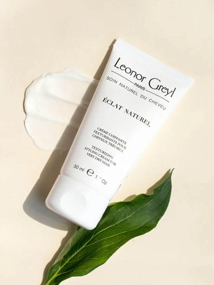 Tube of Leonor Greyl 'Éclat Naturel' with a leaf and product texture swatch on a beige background | Twentyseven Toronto