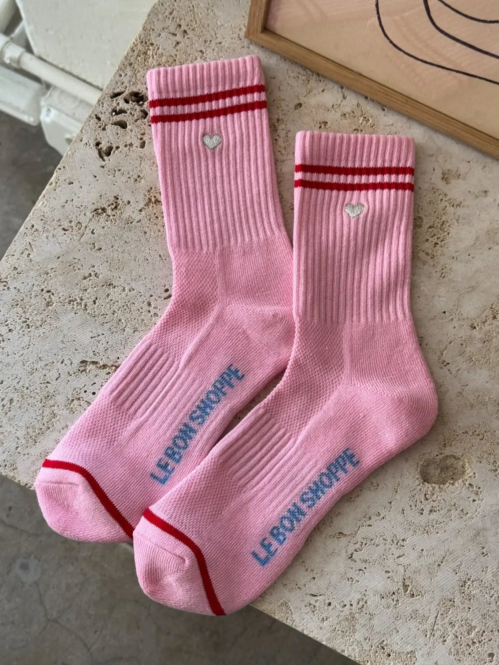 Pair of pink 'Boyfriend Socks' with red stripes and a silver embroidered heart in 'Parchment + Heart' style from Le Bon Shoppe on a marble background | Twentyseven Toronto