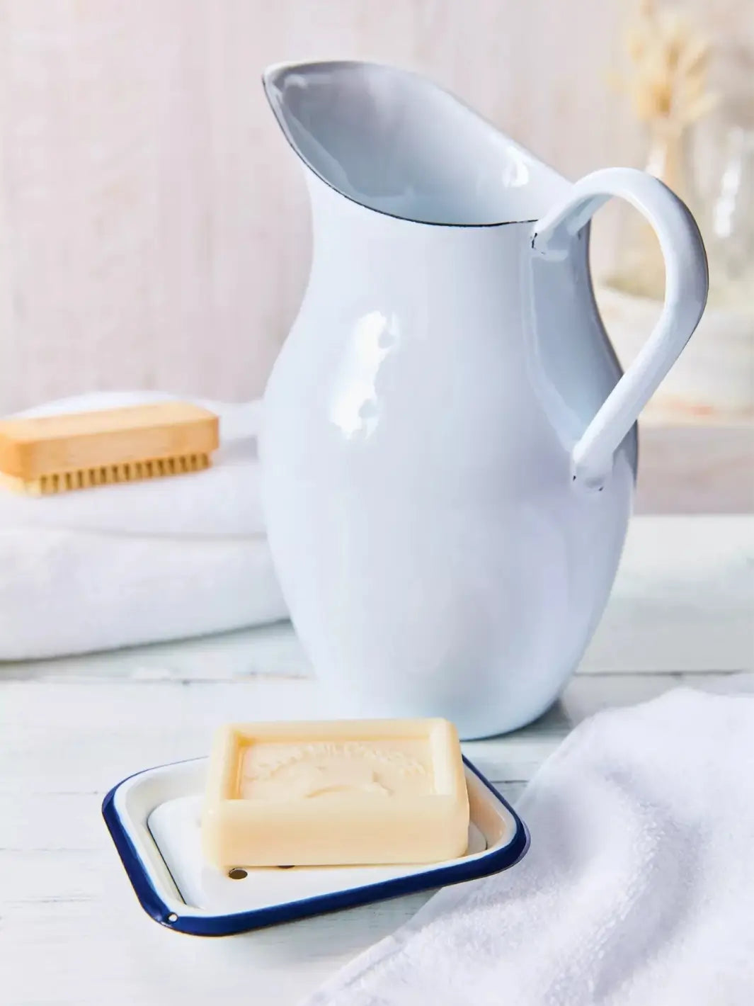 White ceramic pitcher on a white surface with rectangular white soap dish with blue rim from Burstenhaus Redecker and a white towel | Twentyseven Toronto 
