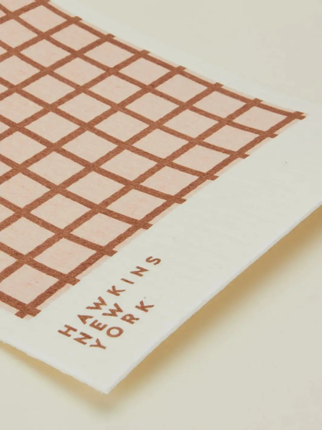 A close-up shot focuses on the texture and brand logo of a red and blush striped sponge cloth from the Essential Swedish Dishcloth in Blush/Terracotta (Set of 6) from Hawkins New York | Twentyseven Toronto