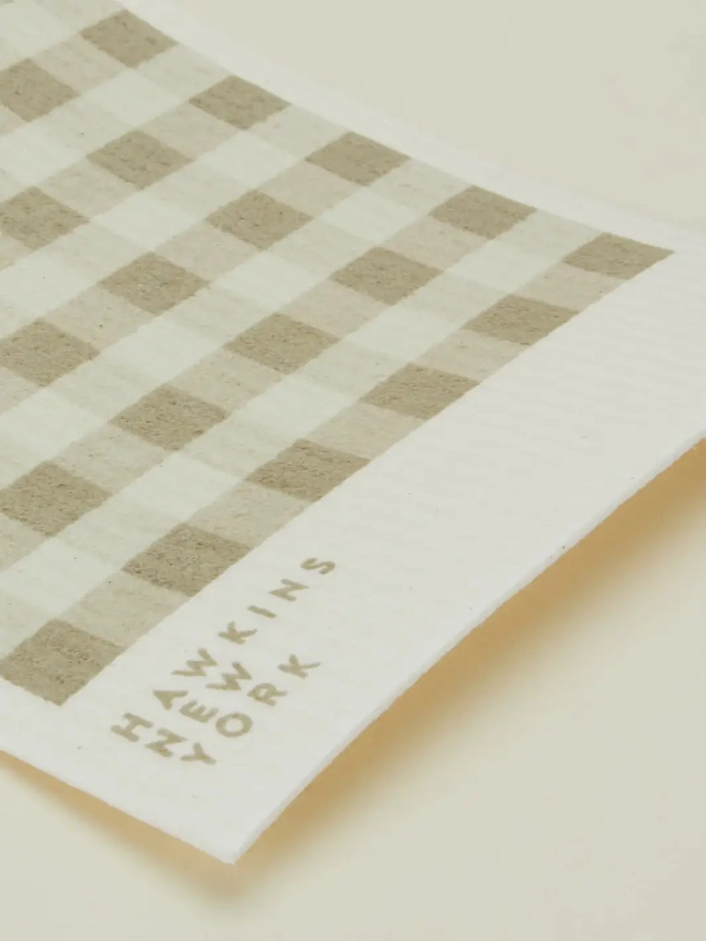 A close-up shot focuses on the texture and brand logo of an ivory and cream striped sponge cloth from the Essential Swedish Dishcloth in Ivory/Flax (Set of 6) from Hawkins New York | Twentyseven Toronto