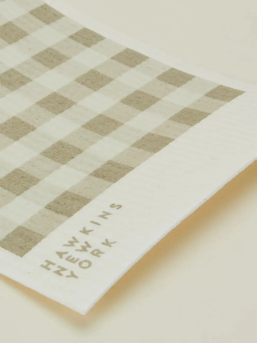 A close-up shot focuses on the texture and brand logo of an ivory and cream striped sponge cloth from the Essential Swedish Dishcloth in Ivory/Flax (Set of 6) from Hawkins New York | Twentyseven Toronto