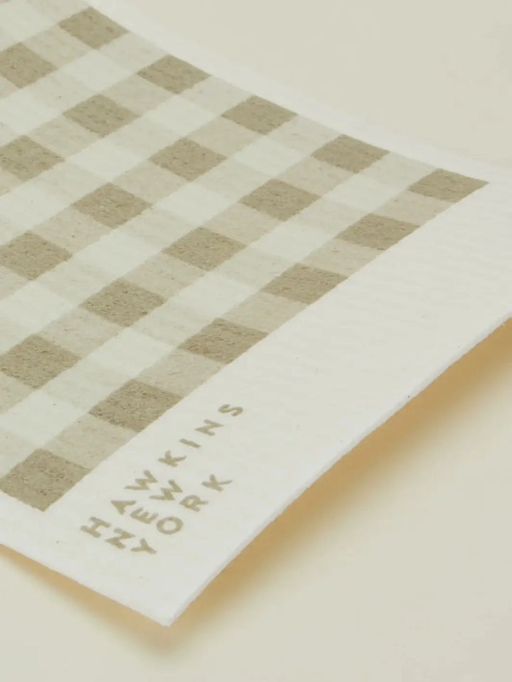 A close-up shot focuses on the texture and brand logo of an ivory and cream striped sponge cloth from the Essential Swedish Dishcloth in Ivory/Flax (Set of 6) from Hawkins New York | Twentyseven Toronto