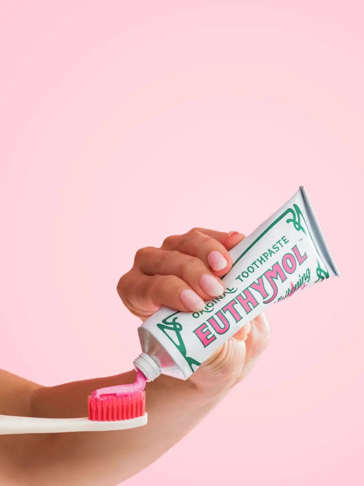 Person squeezes a vibrant pink paste from a tube of Euthymol Original Whitening Pink Japanese Toothpaste directly onto a matching pink-bristled toothbrush against a soft pink background | Twentyseven Toronto