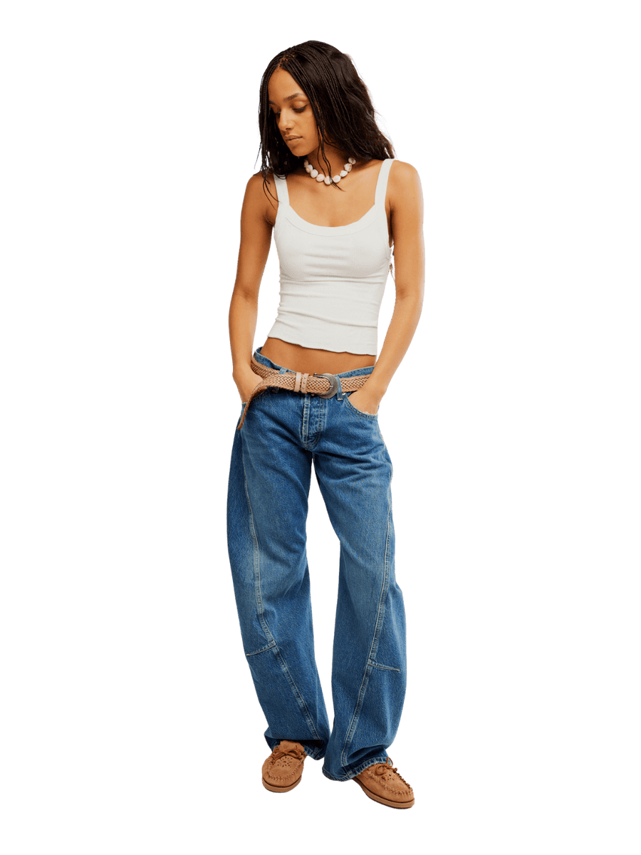 A model with braided hair wearing the Free People Fable Twisted Seam Jean in Heartsong, a white tank top, and a woven belt | Twentyseven Toronto