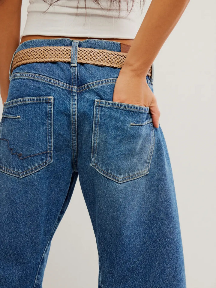 A close-up back view details the woven brown belt and right back pocket of the Free People Fable Twisted Seam Jean in Heartsong with a hand partially tucked inside | Twentyseven Toronto