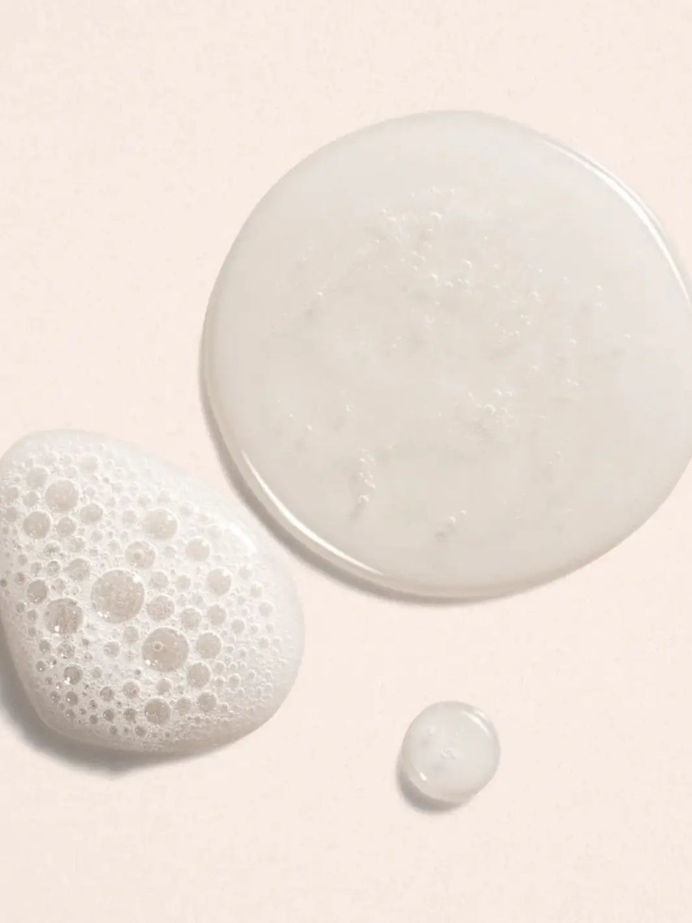 Three white product drops of Beauty from Bees Face Cleanser with textured surfaces on a light pink background | Twentyseven Toronto