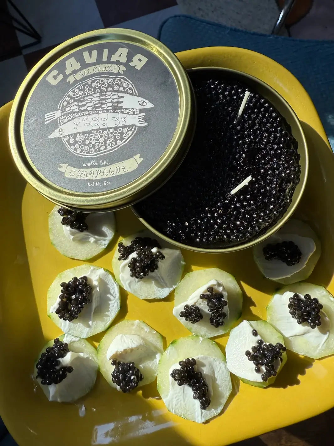 Fancy Caviar Candle in a gold and black tin from Tinned Fish Candles on a yellow plate | Twentyseven Toronto