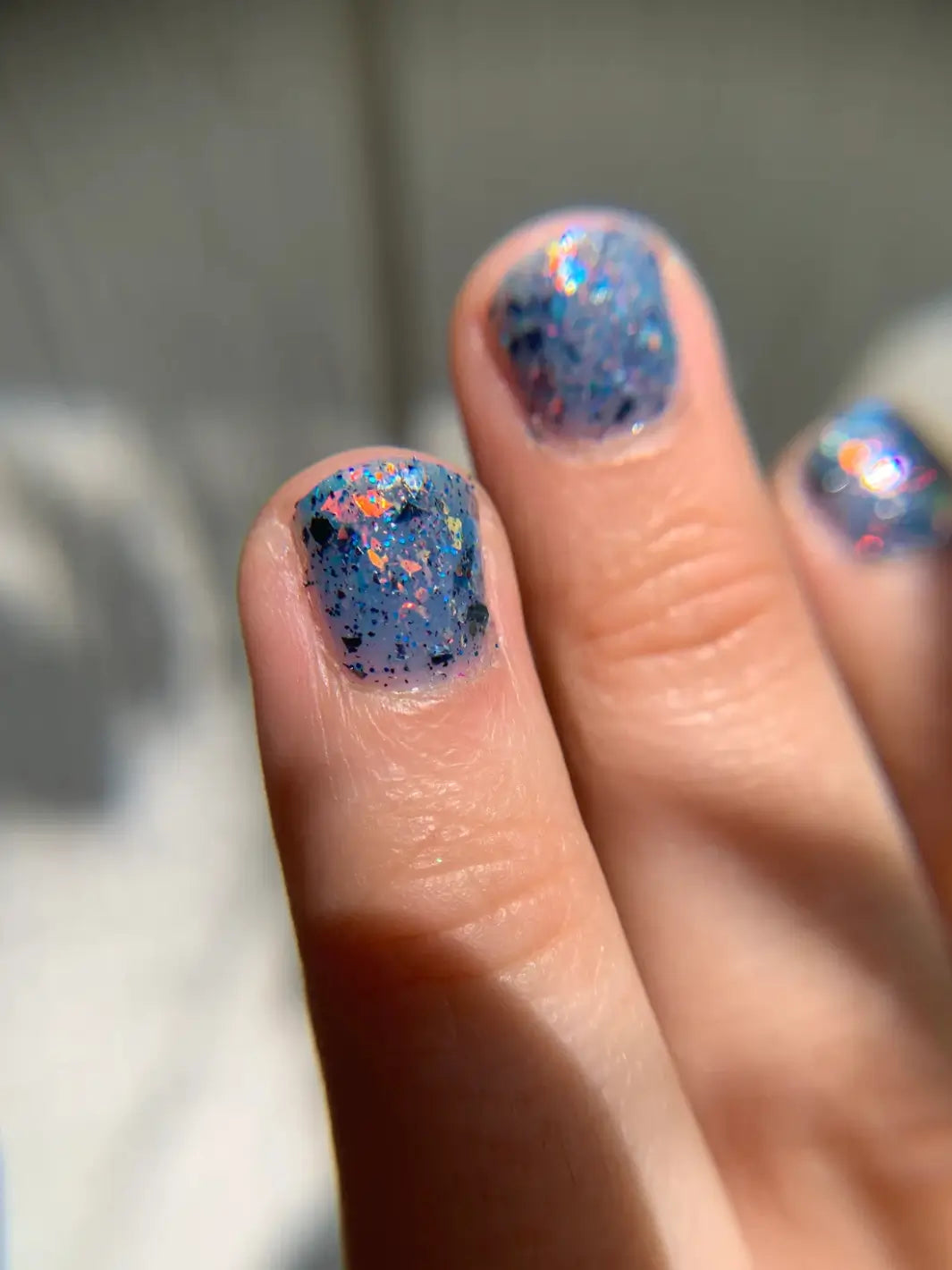 A close-up shot under direct light shows short, rounded fingernails painted with Death Valley Nails Fish Scales Nail Polish, emphasizing the concentrated cluster of fiery orange iridescent flakes | Twentyseven Toronto