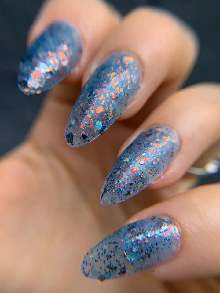 A close up of a hand with long, pointed nails captures the multi-dimensional blue, speckled finish of Death Valley Nails Fish Scales Nail Polish | Twentyseven Toronto