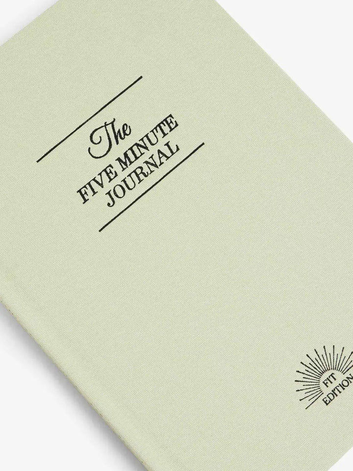 A close-up shot focuses on the cover text and "Fit Edition" logo embossed on the front of the light green Intelligent Change The Five Minute Journal Health & Fitness Edition | Twentyseven Toronto