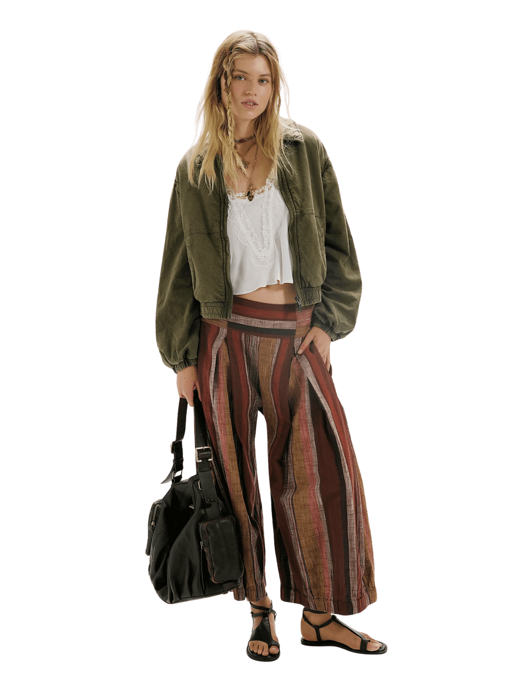 A model stands wearing a distressed olive green FP One Birdie Washed Jacket from Free People, a white cropped tank top, wide-leg striped pants in red, brown, and beige, and carrying a black duffel bag | Twentyseven Toronto