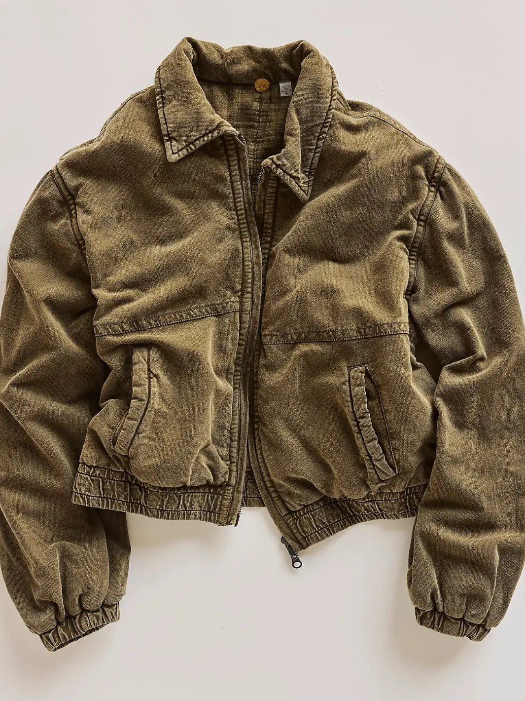An olive green corduroy FP One Birdie Washed Jacket from Free People with a zippered front, collar, and elasticized cuffs, laid flat against a light off-white background | Twentyseven Toronto