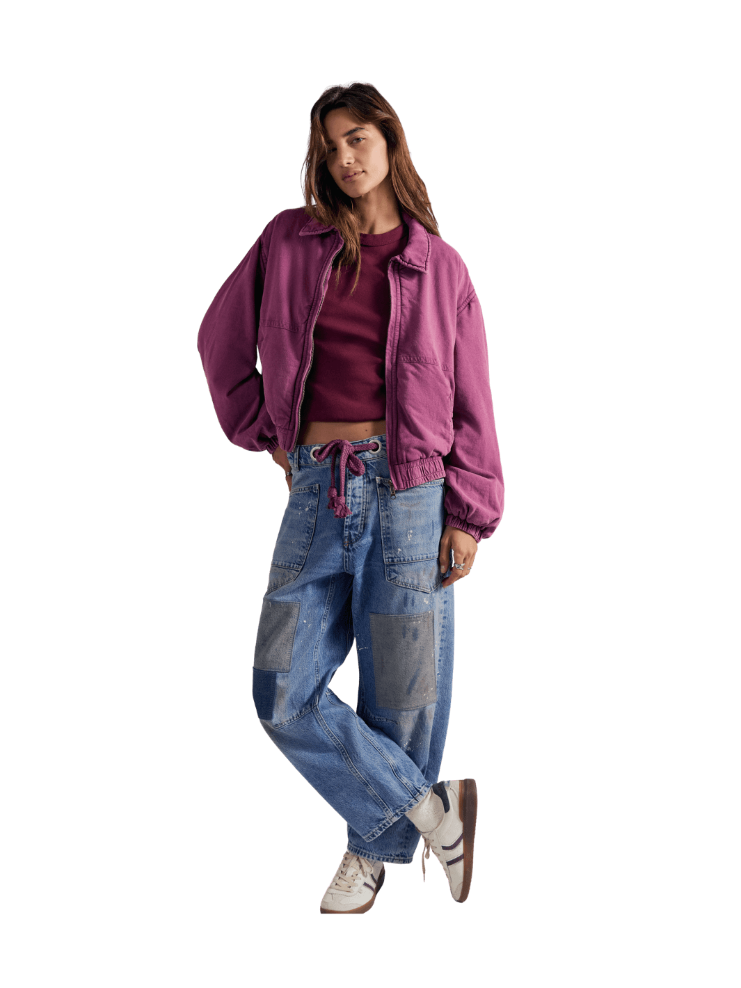 A model wearing a purple cropped bomber FP One Birdie Washed Jacket in Roan Rouge from Free People over a dark red crop top, paired with light blue patchwork denim jeans and white sneakers | Twentyseven Toronto