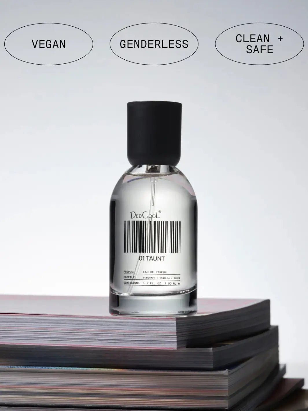 A full-size 50ml bottle of Dedcool Fragrance 01 "Taunt" resting on a stack of magazines beneath labels reading "Vegan," "Genderless," and "Clean + Safe" | Twentyseven Toronto