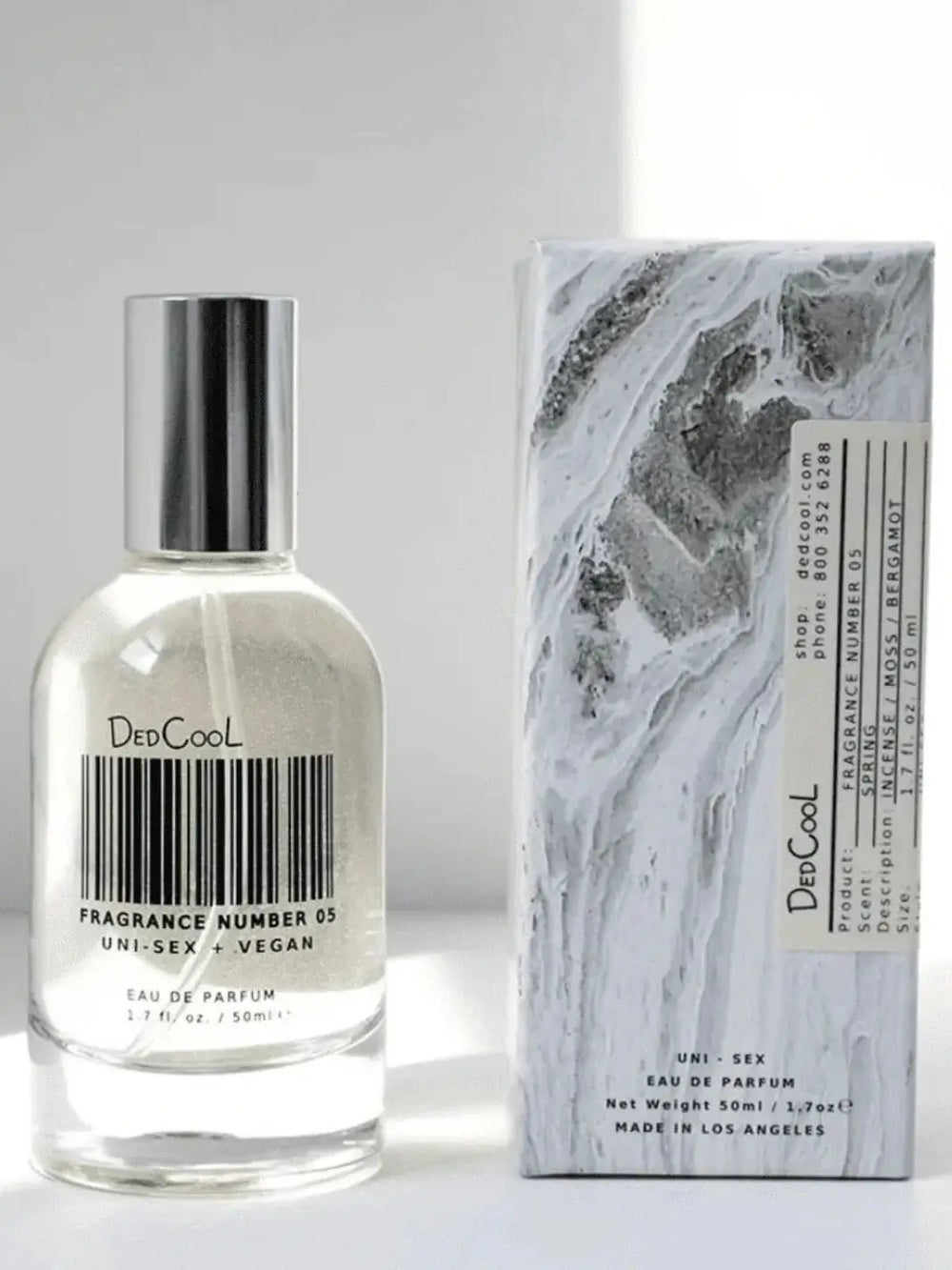 A clear glass bottle of Dedcool Fragrance 05 "Spring" with a barcode design on the label stands next to its marble-patterned product box | Twentyseven Toronto