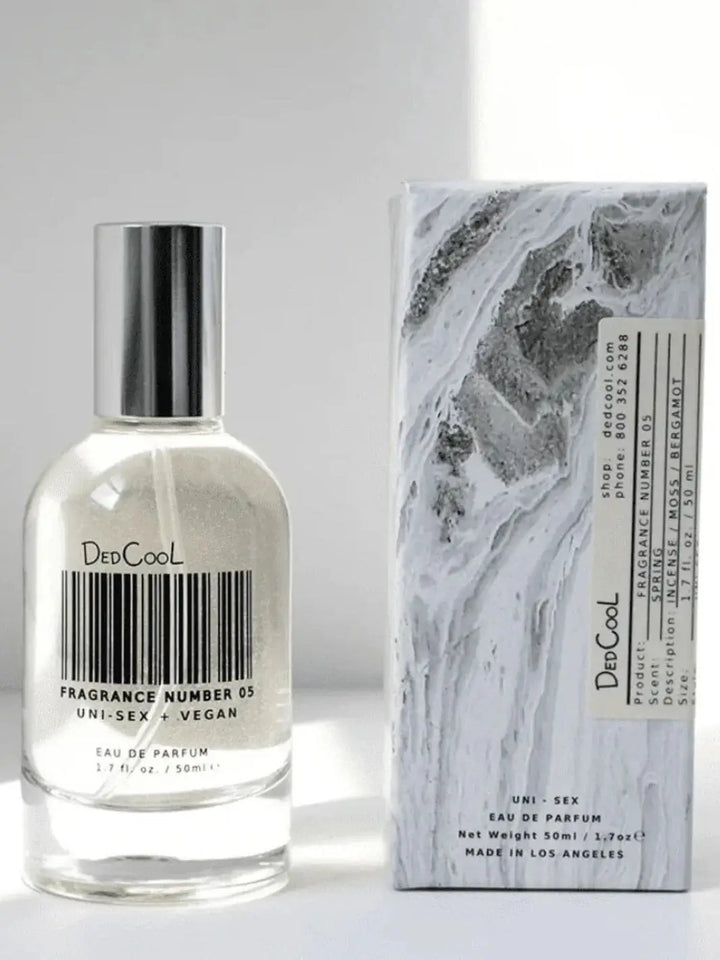 A clear glass bottle of Dedcool Fragrance 05 "Spring" with a barcode design on the label stands next to its marble-patterned product box | Twentyseven Toronto