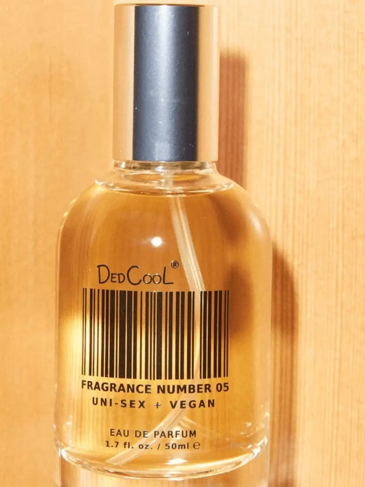A close-up shot shows a 50ml glass bottle of Dedcool Fragrance 05 "Spring" filled with amber-colored liquid against a warm wood background | Twentyseven Toronto