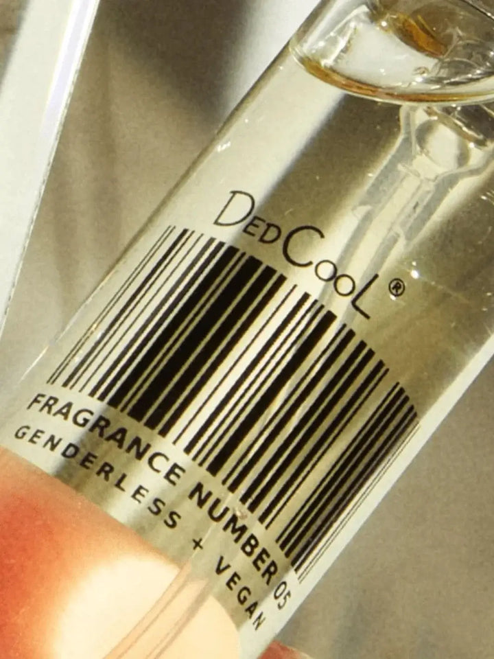 An extreme close-up highlights the barcode label on a glass bottle of Dedcool Fragrance 05 "Spring," emphasizing the text "Fragrance Number 05 Genderless + Vegan." | Twentyseven Toronto