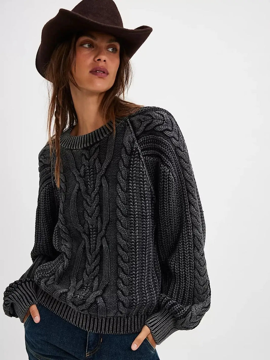 A three-quarter front view displays a model wearing the slouchy, oversized Free People Frankie Cable Sweater in Black with dark denim jeans and a brown fedora | Twentyseven Toronto
