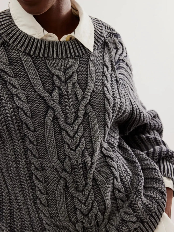 A detailed close-up shot emphasizes the prominent center-front cable knit motifs and ribbed collar of the Free People Frankie Cable Sweater in Black layered over a white collared shirt | Twentyseven Toronto