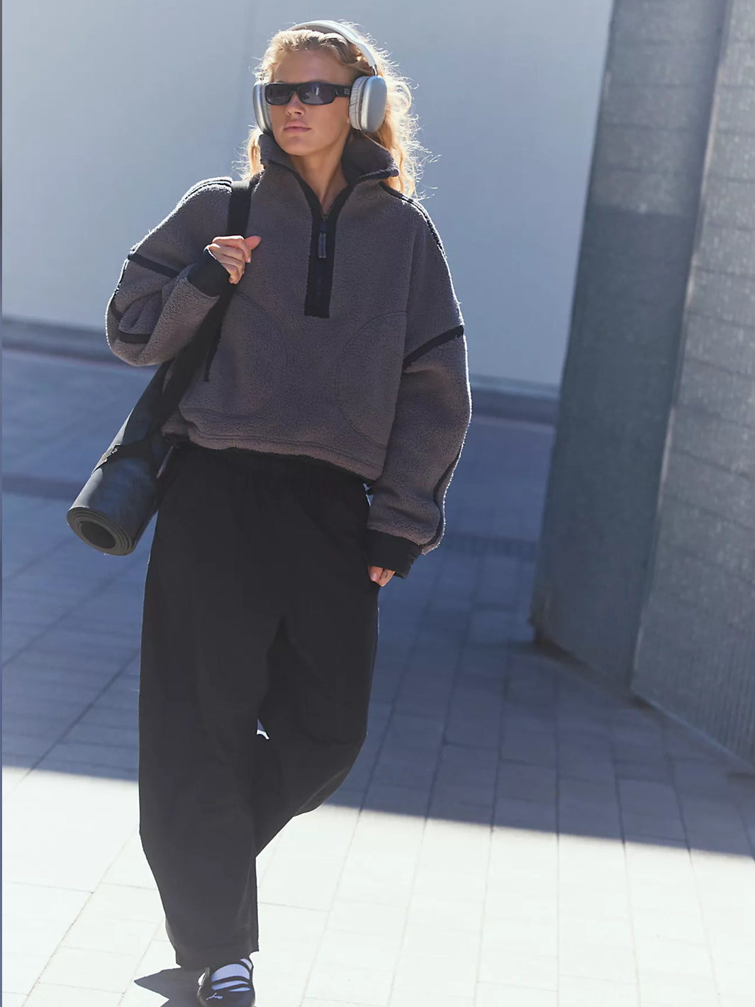 Full-length model wearing a charcoal grey sherpa half-zip pullover with black trim, black wide-leg pants, oversized headphones, and sunglasses while carrying a yoga mat and tote bag outdoors  Twentyseven Toronto