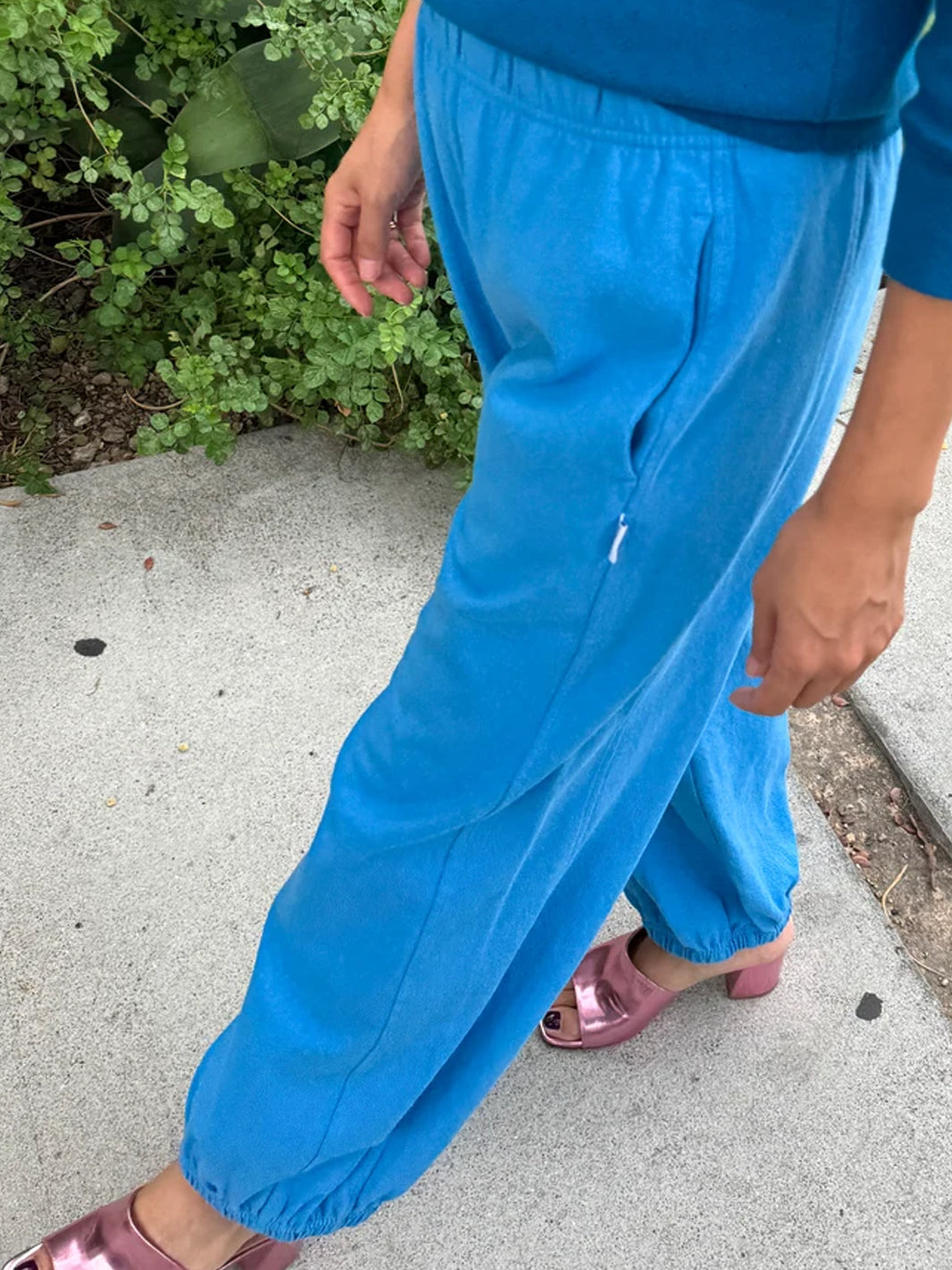Side view of French Blue Balloon Pants featuring a loose balloon silhouette, side pockets and elasticated ankle cuffs, paired with a matching blue sweater and metallic pink heels | Twentyseven Toronto