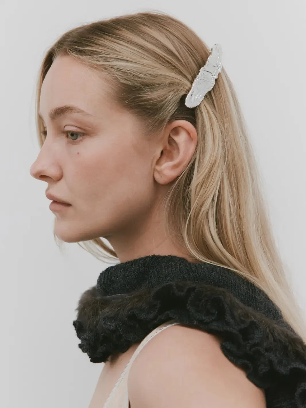 Side profile of a blonde model styling her hair half-up with the textured, silver Frida Barrette in Silver from Wolf Circus | Twentyseven Toronto