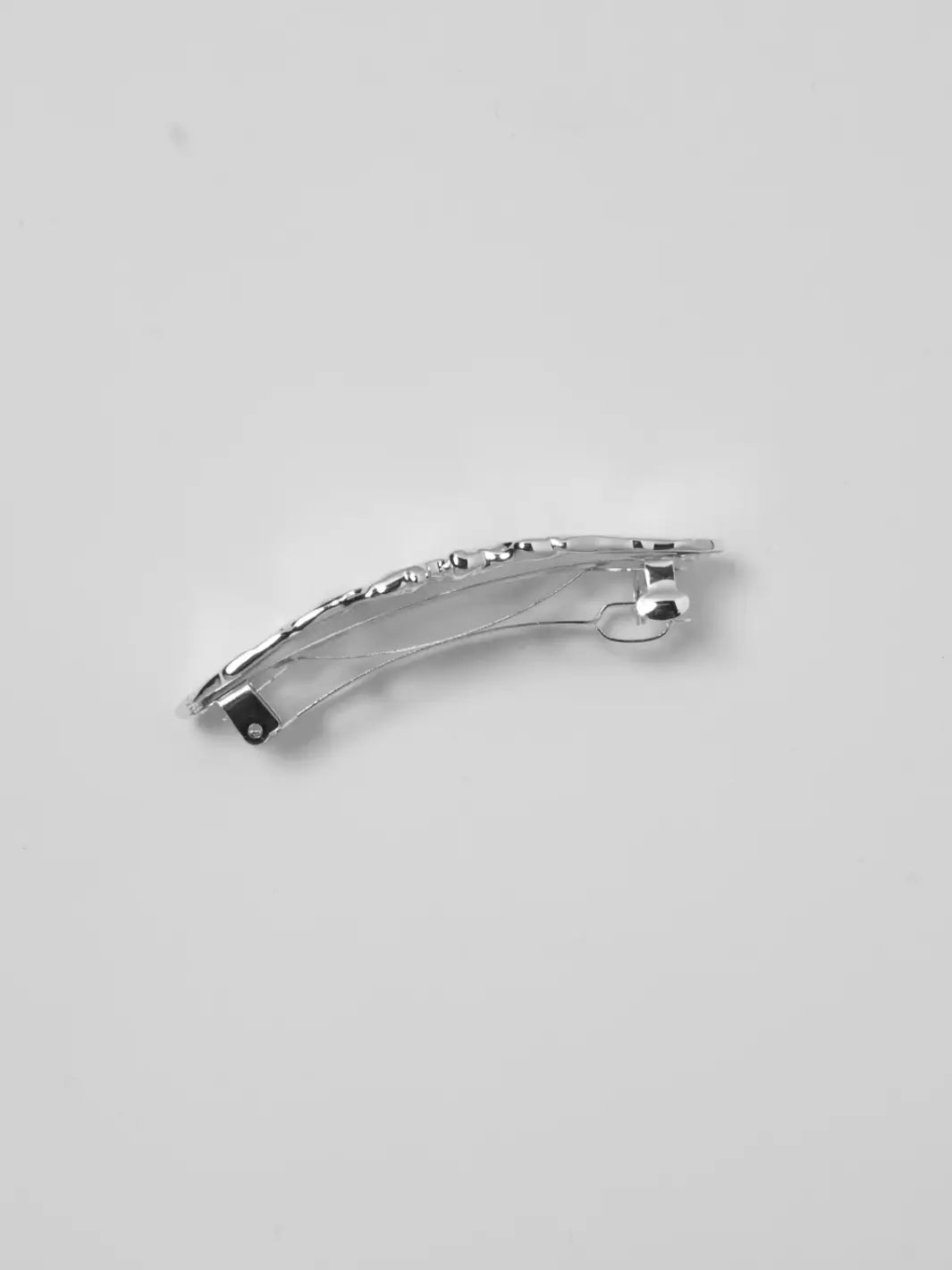 The Frida Barrette in Silver from Wolf Circus on a gray background, showcasing its curved shape and classic metal clip mechanism underneath | Twentyseven Toronto