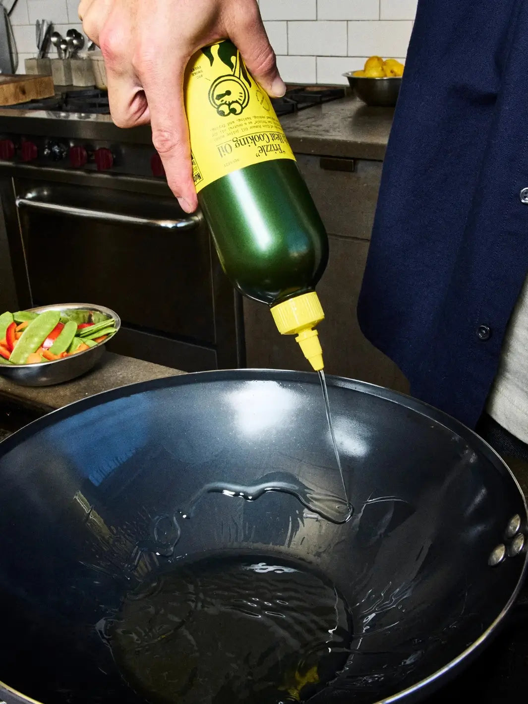 Person pouring oil from Graza 'Frizzle' High Heat Cooking Oil bottle into a black frying pan in a kitchen | Twentyseven Toronto