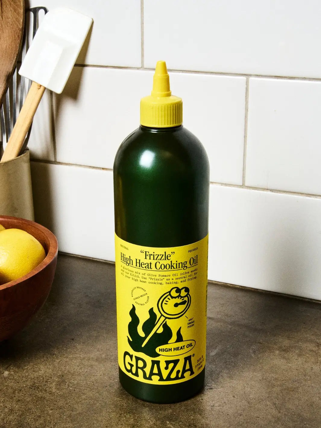 Bottle of Graza 'Frizzle' high heat cooking oil with yellow label on a kitchen counter | Twentyseven Toronto