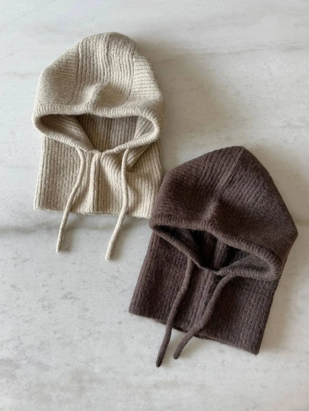 Two ribbed Billy Bamboo Fuzzy Alpaca Balaclava hoods, one in light beige and one in dark brown, are laid flat face-up on a white marble surface | Twentyseven Toronto