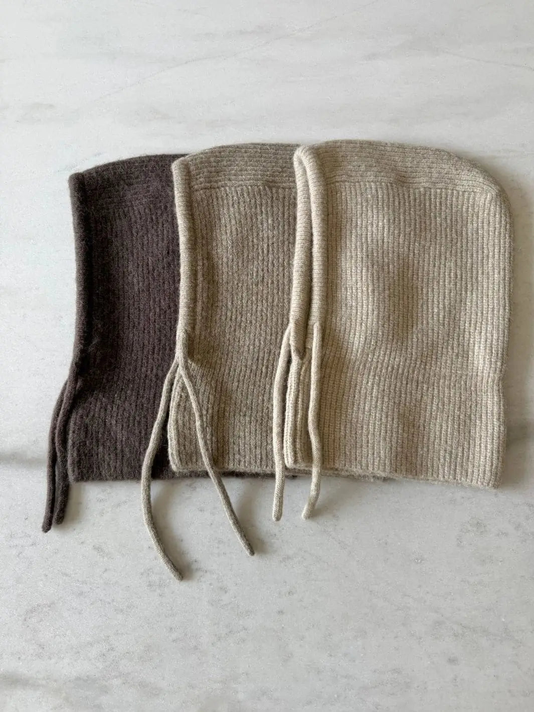 Three Billy Bamboo Fuzzy Alpaca Balaclava hoods in dark brown, taupe, and light beige are layered in a profile view showing their side silhouettes on a marble countertop | Twentyseven Toronto
