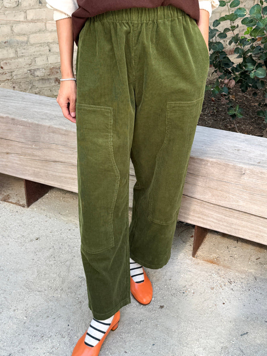 Model wearing Le Bon Shoppe Corduroy Gardener's Pants in Bay Leaf green, featuring a relaxed fit, elastic waistband and oversized carpenter-inspired patch pockets, styled with orange shoes | Twentyseven Toronto