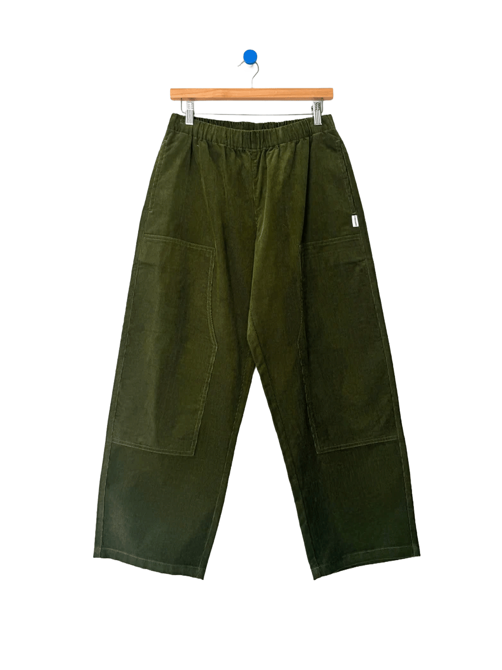Le Bon Shoppe Corduroy Gardener's Pants in Bay Leaf on a wooden hanger against a white background, featuring an elastic waistband, oversized patch pockets and relaxed tapered legs | Twentyseven Toronto