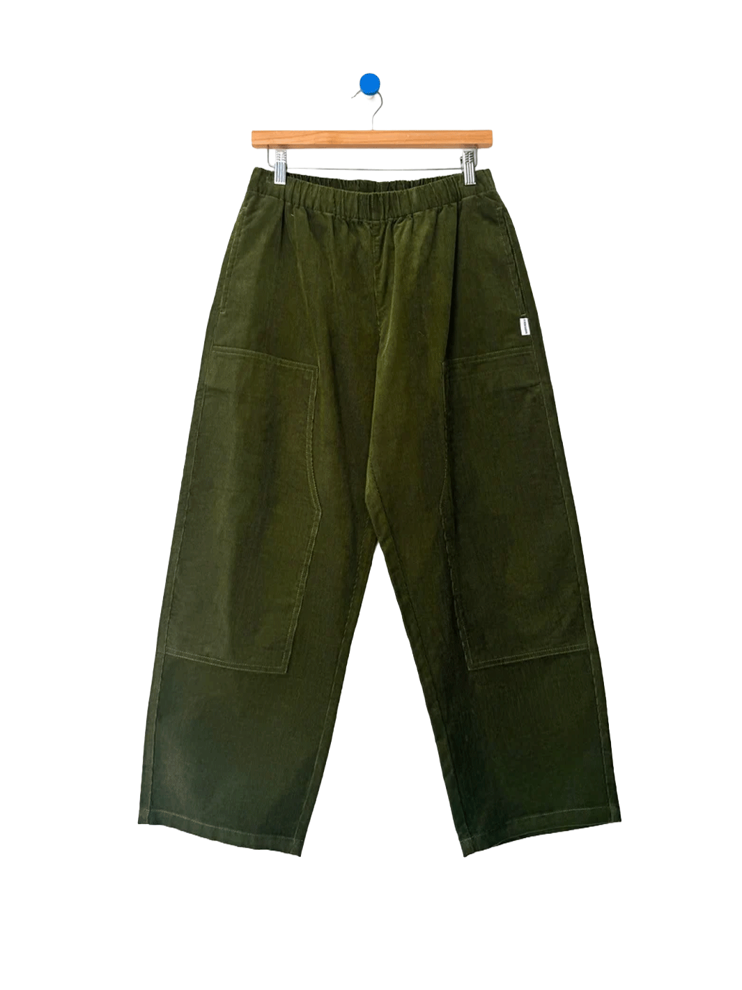 Le Bon Shoppe Corduroy Gardener's Pants in Bay Leaf on a wooden hanger against a white background, featuring an elastic waistband, oversized patch pockets and relaxed tapered legs | Twentyseven Toronto